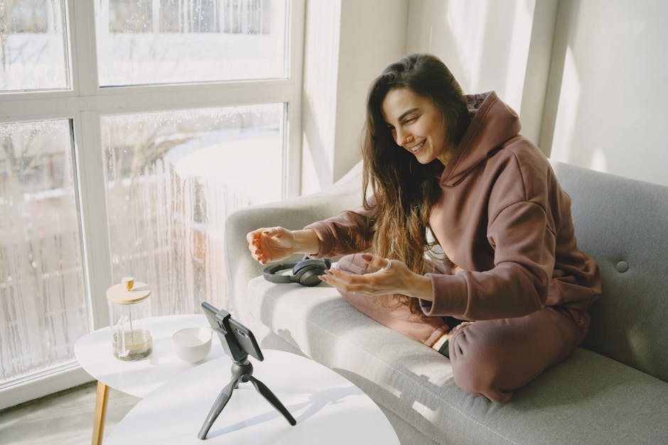 Young woman vlogging at home, using smartphone and tripod while sitting on a couch.