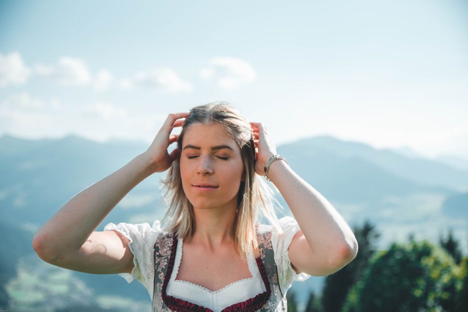 A serene woman in traditional attire enjoys the stunning Kitzbühel mountain scenery.