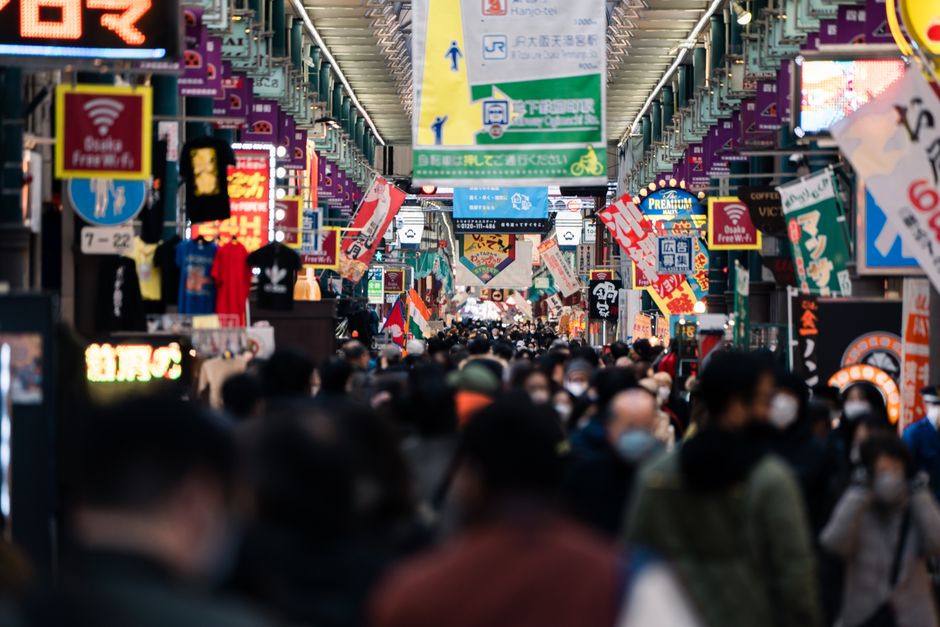Vibrant street scene in Osaka's Dotonbori area, bustling with locals and tourists under colorful signage.