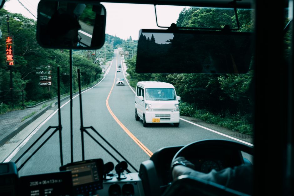 View from inside a bus on a scenic road with greenery and passing white van.