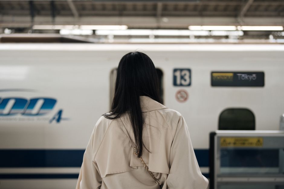 A woman waits at a Tokyo train station, facing a high-speed bullet train, symbolizing travel and anticipation.