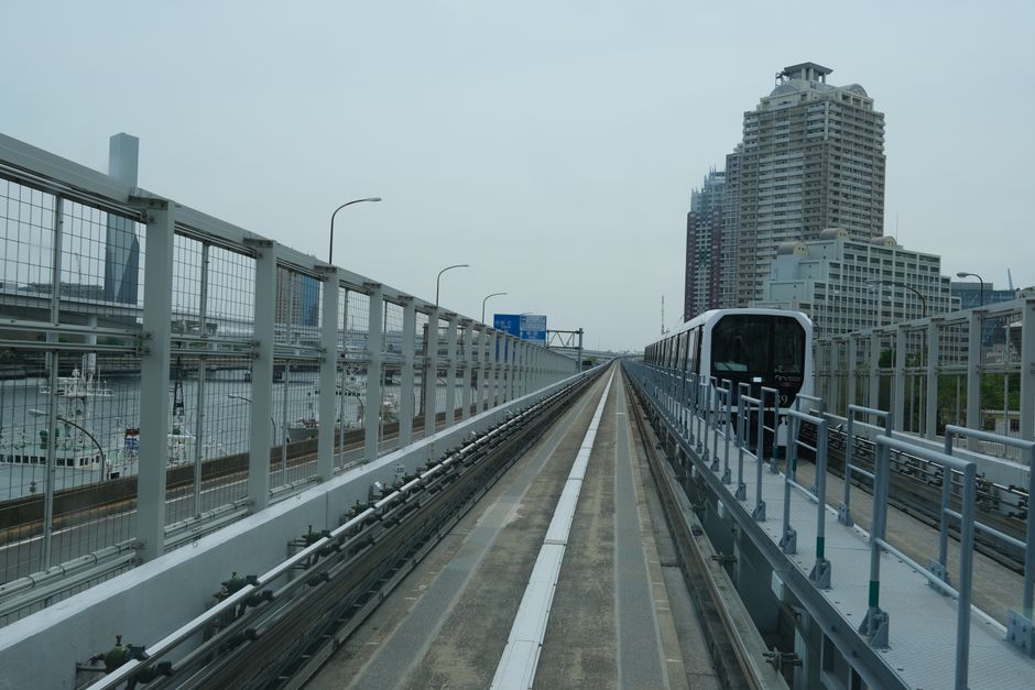 Driverless train moves through Tokyo's modern architecture with skyscrapers in view.