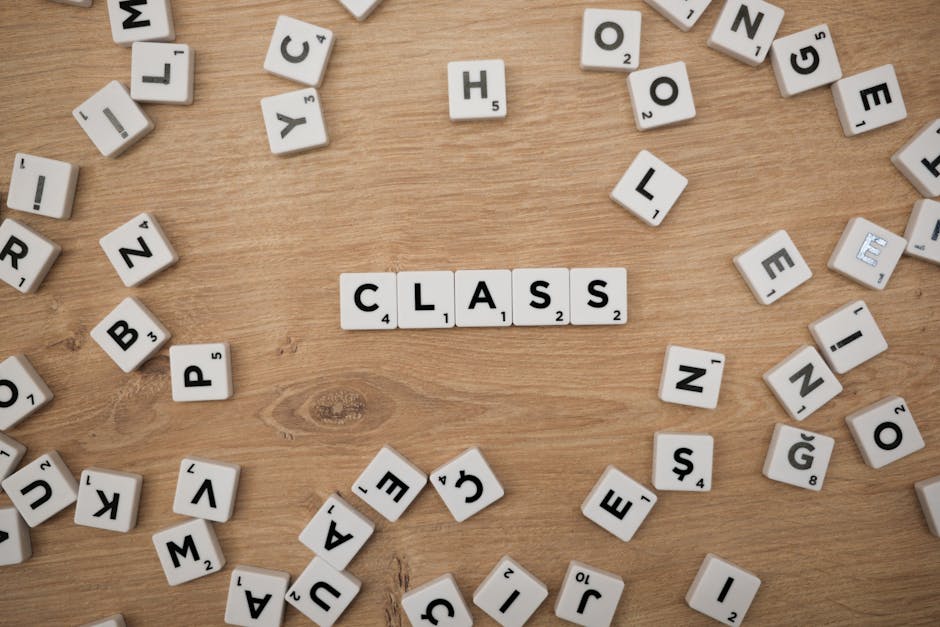 Scrabble letter tiles spelling 'class' on a wooden table amidst scattered tiles.