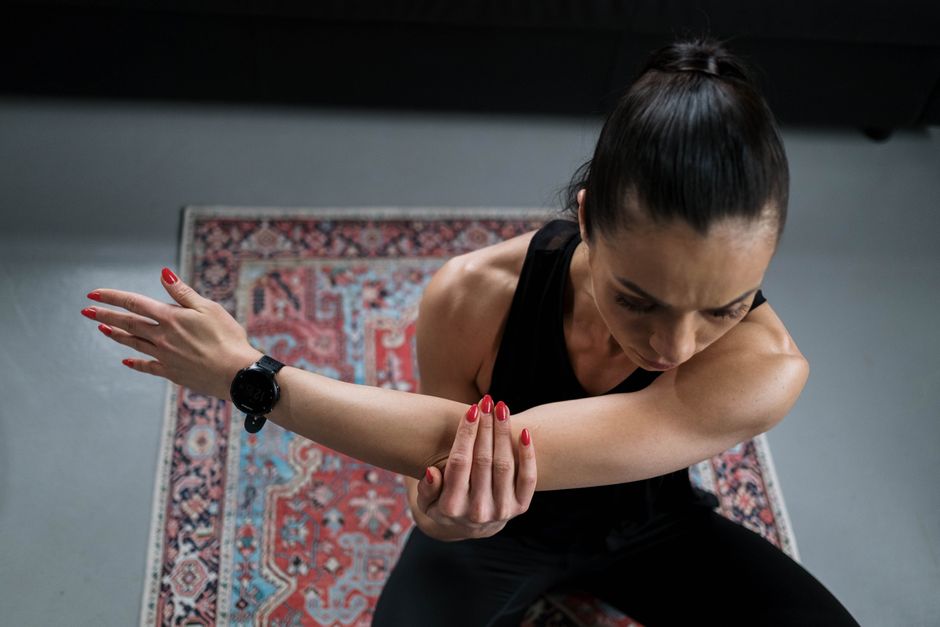 Woman practicing stretching indoors, focusing on fitness and wellness with a colorful rug backdrop.