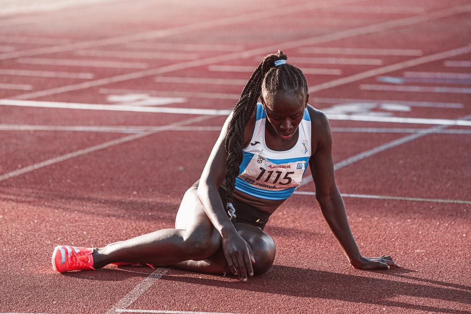 A female athlete in sports gear taking a break on the running track after a race, during daylight.