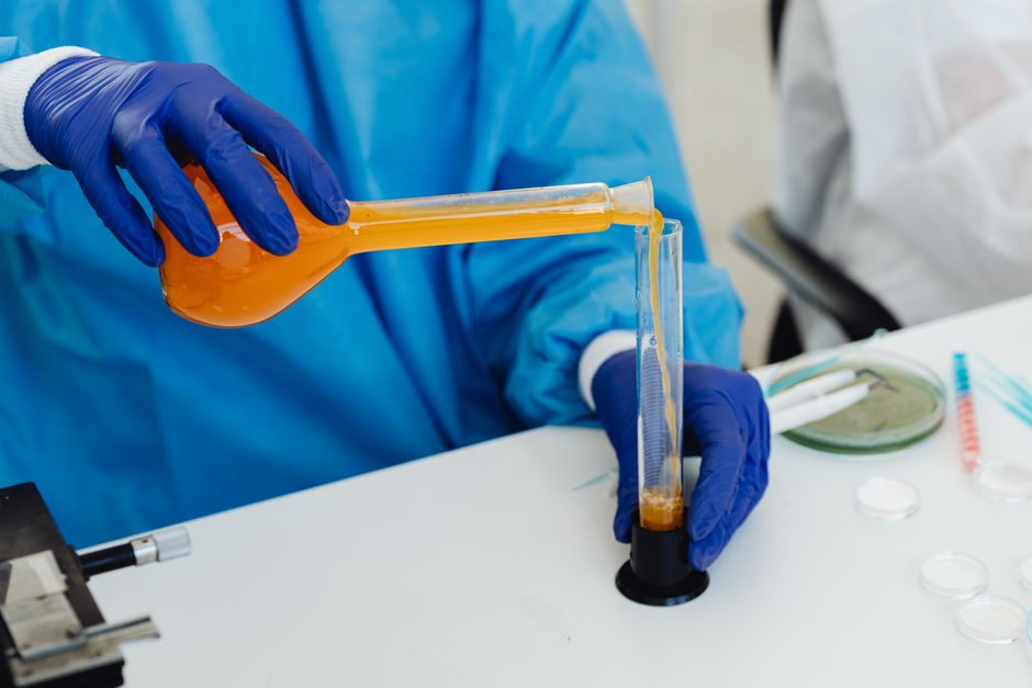 Close-up of a scientist pouring orange liquid into a vial in a laboratory setting.