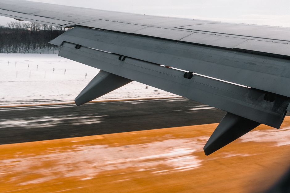 Close-up of an airplane wing during landing on a snowy runway, showcasing aviation dynamics.